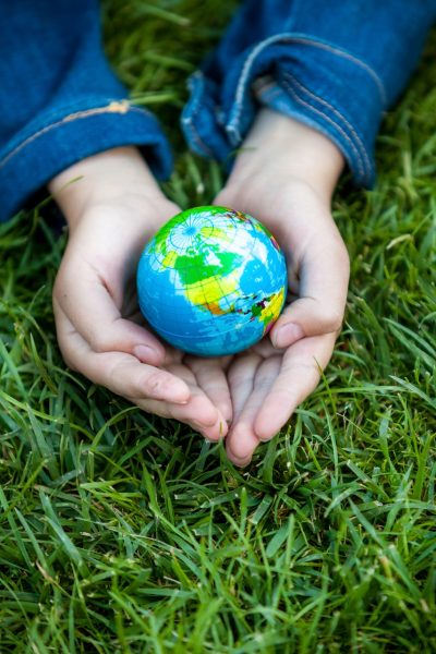 girl holding Earth in hands against green grass Young girl holding Earth in hands against green grass